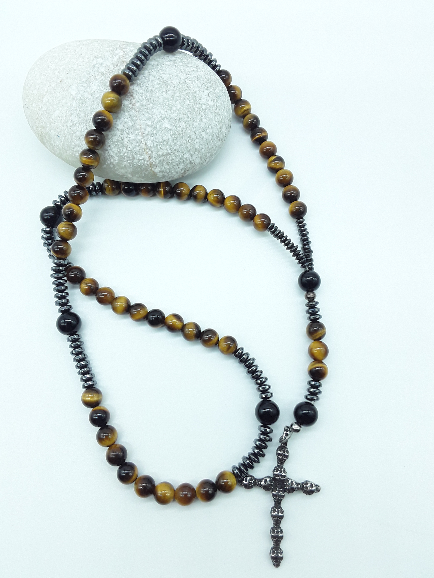 Catholic rosary with tiger’s eye beads, black onyx elements, and a stainless steel skull cross shown in full length on a light background.