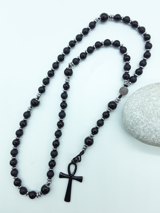 Onyx and Hematite Ankh Catholic Rosary (5 Decade) by Polmadeva placed beside natural stone with black cross.