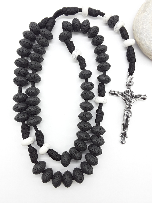 Lava and Howlite Paracord Catholic Rosary (5 Decade) by Polmadeva placed beside natural stone with stainless steel crucifix.