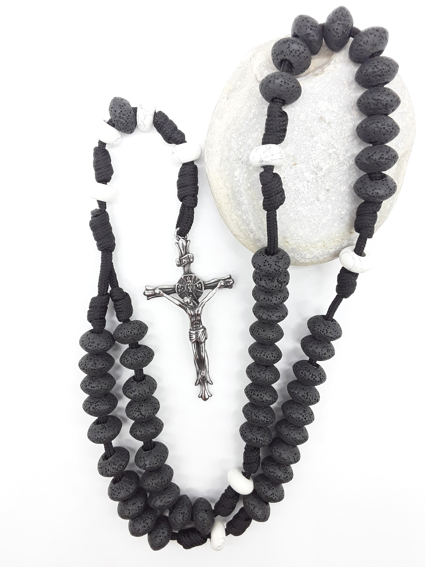 Lava and Howlite Paracord Catholic Rosary (5 Decade) by Polmadeva resting on natural stone surface with stainless steel crucifix.