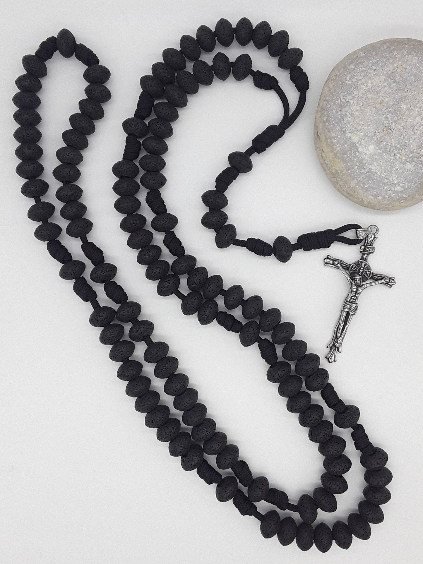 Lava stone Catholic Paracord Rosary placed beside natural stone, expressing endurance, weight, and grounded prayer through repetition