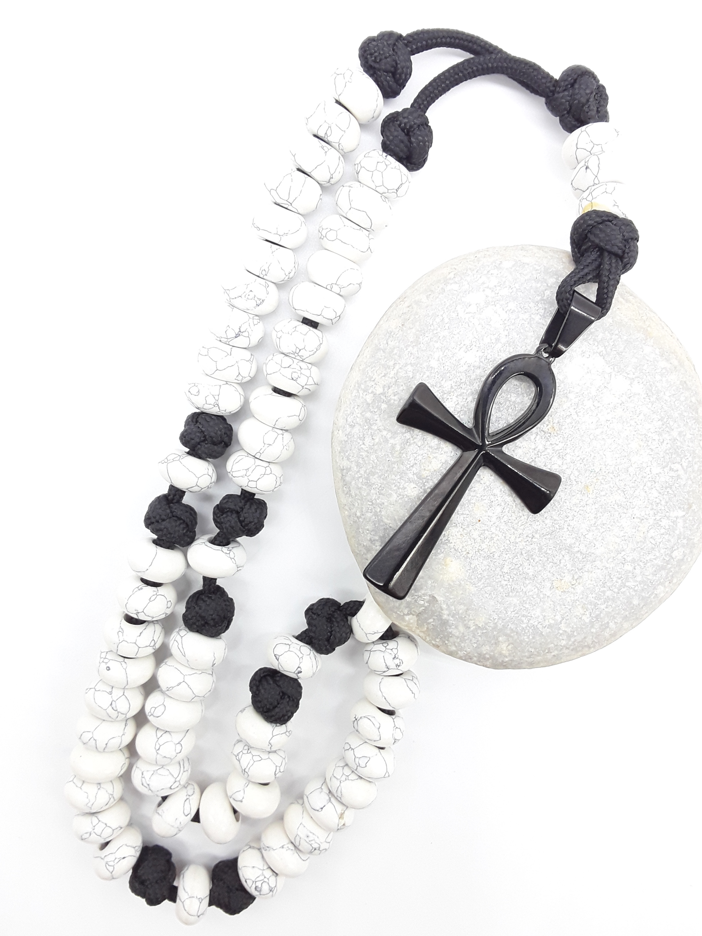 Howlite Paracord Catholic Rosary with Ankh cross by Polmadeva placed beside natural stone, 5-decade design.