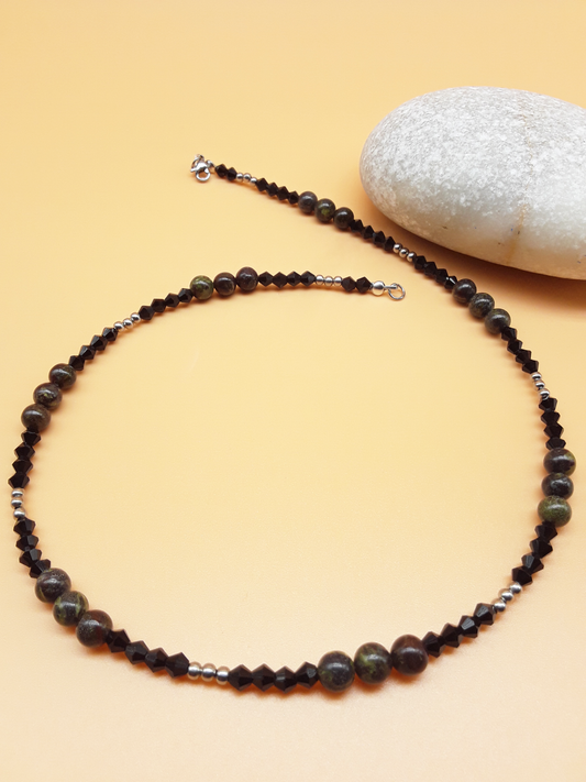 Still a Wonder Dragon Blood Gemstone, Hematite and Swarovski Crystal necklace with Stainless Steel clasp by POLMADEVA next to a white stone.
