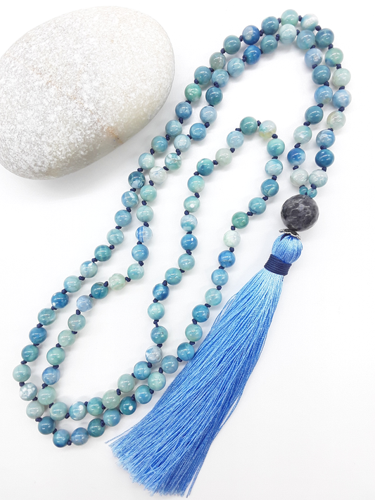 Agate and Labradorite Mala Beads with blue tassel placed beside white stone on white background, Polmadeva