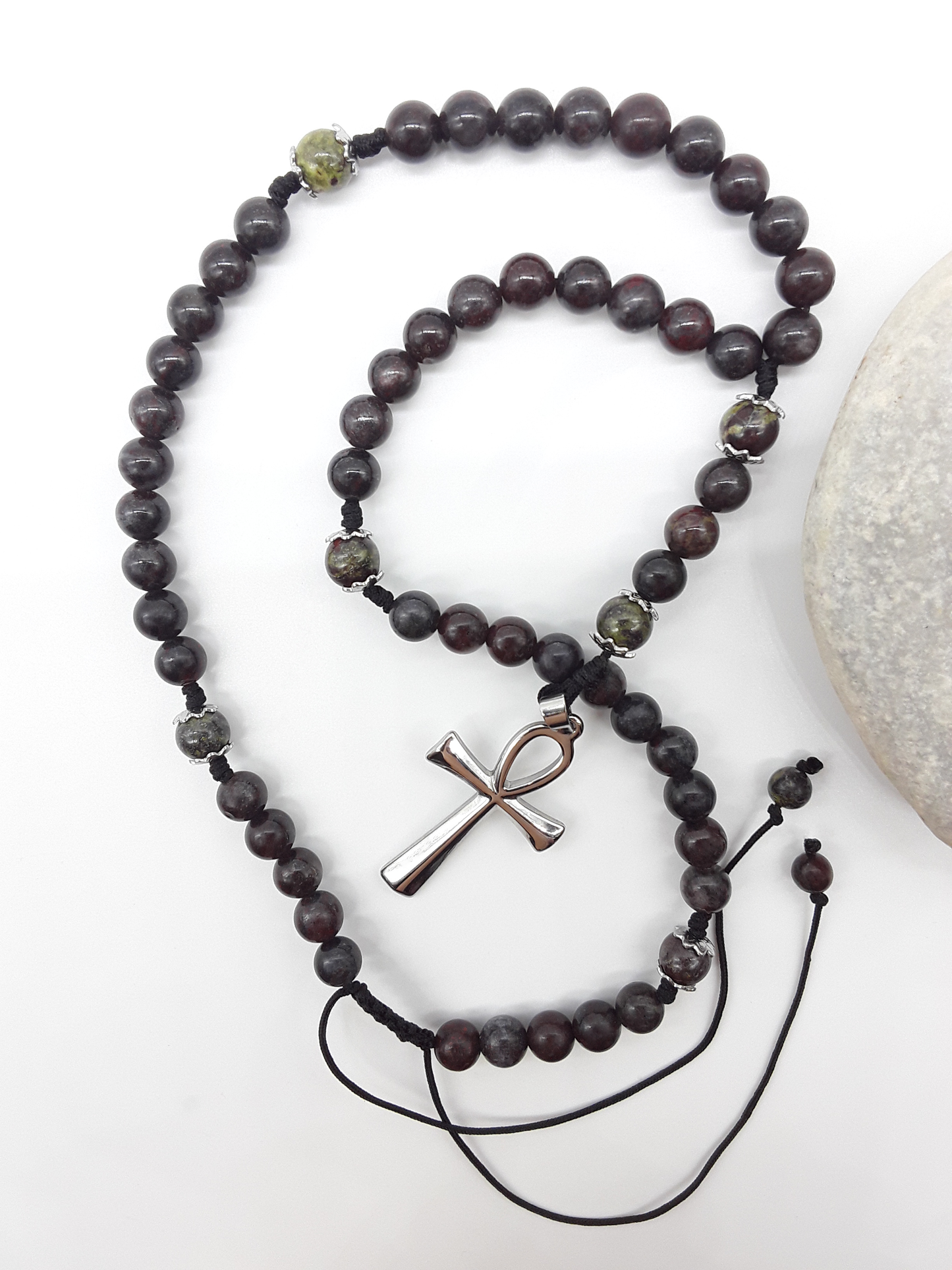Catholic bloodstone rosary with Ankh cross placed beside natural stone on white surface