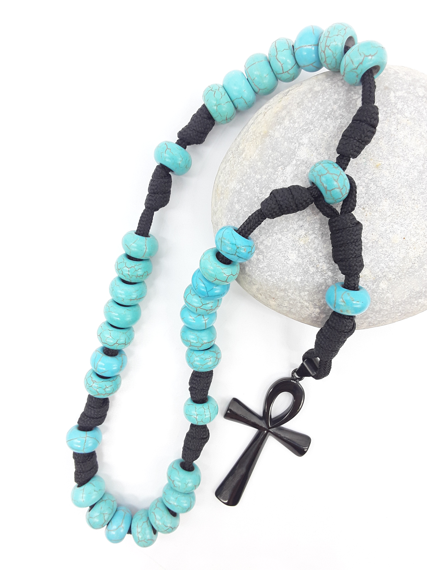 The Living Covenant Paracord Anglican Prayer Beads by Polmadeva placed on stone, crafted with Turquoise and stainless steel Ankh cross