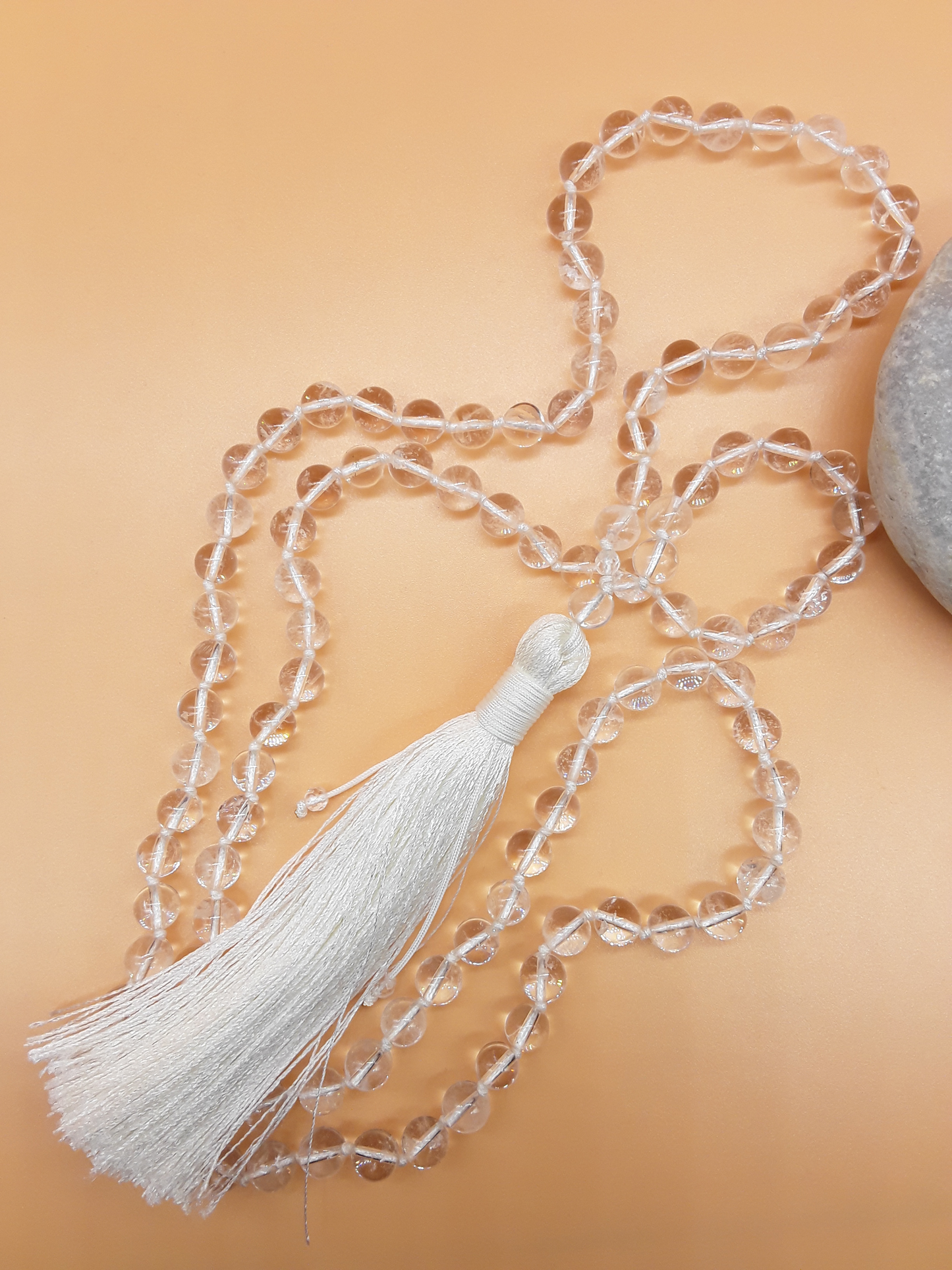 Crystal Quartz Mala Beads with white tassel placed beside white stone on soft background, Polmadeva