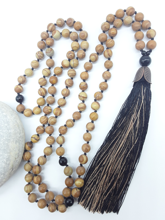 Tigerskin Jasper Mala Beads with Black Onyx details and tassel placed beside white stone on white background, Polmadeva