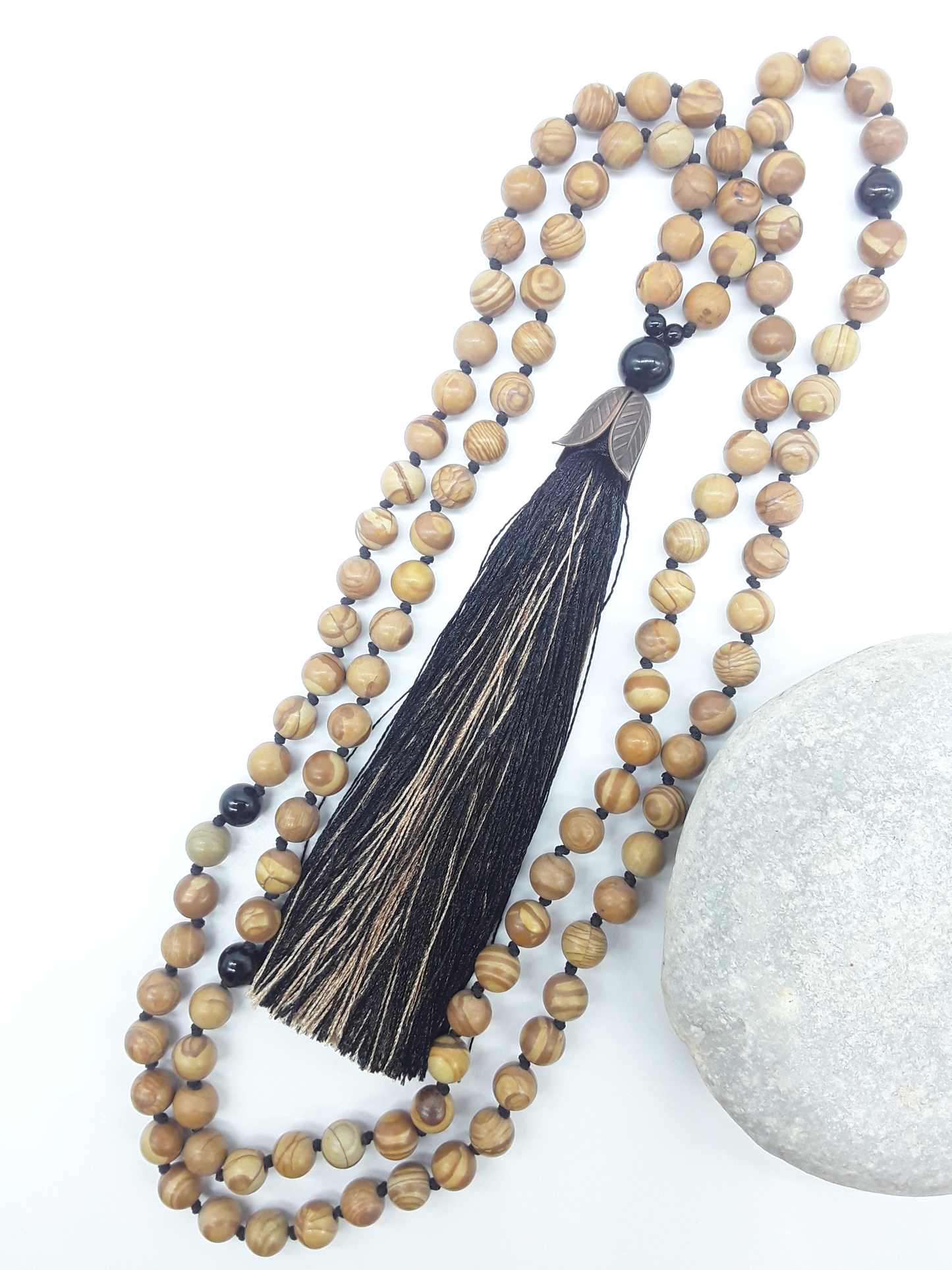 Tigerskin Jasper Mala Beads with Black Onyx arranged in flowing form with tassel next stone on white background, Polmadeva