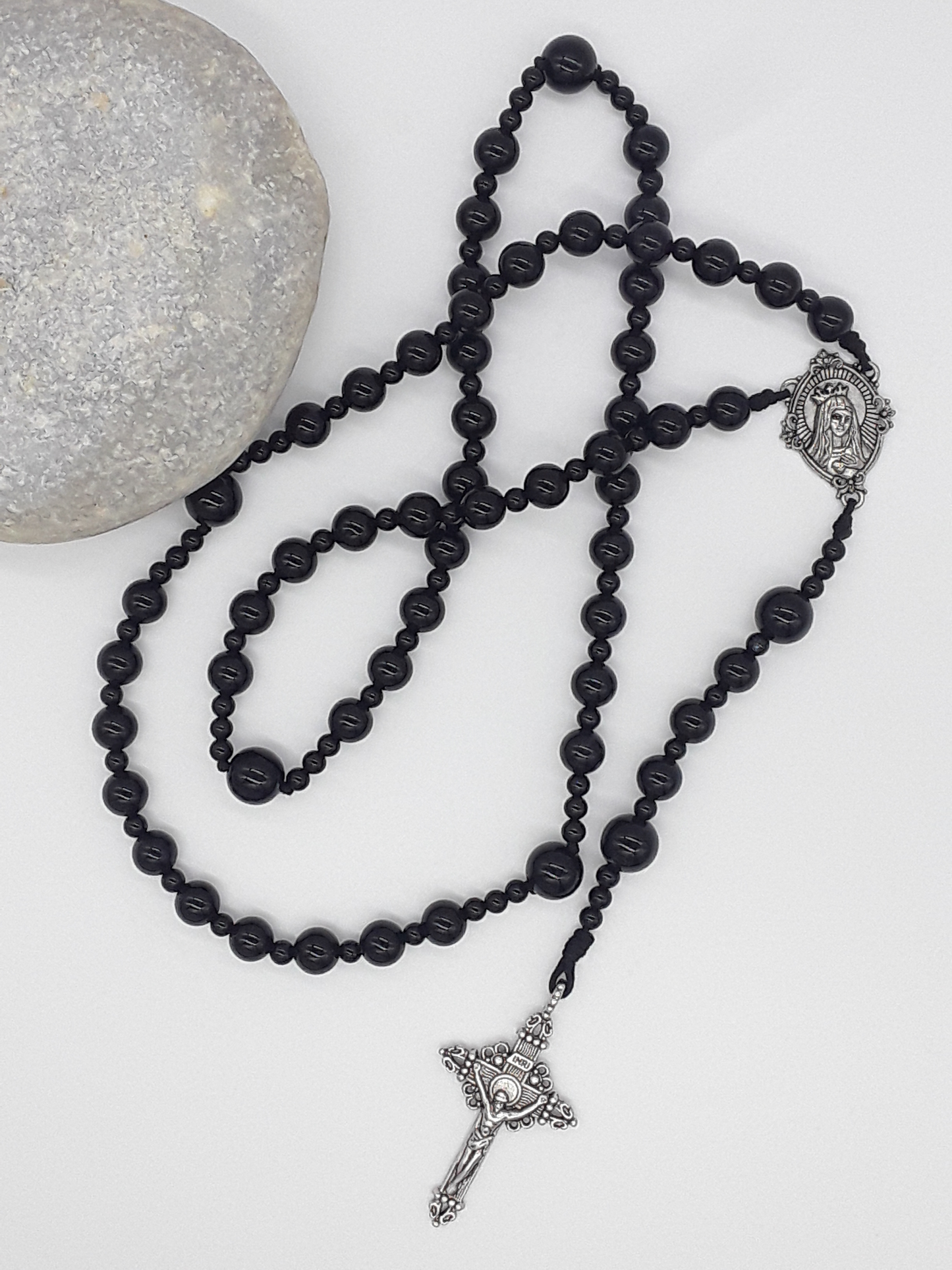 Black onyx Catholic rosary featuring a tin Virgin Mary medallion and traditional tin crucifix, arranged on a light neutral background.