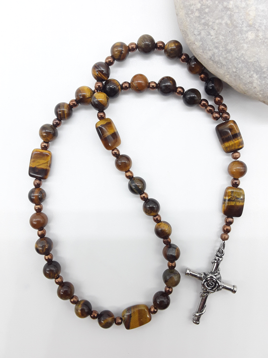 The Steady Gaze Anglican Prayer Beads by Polmadeva beside natural stone, featuring Tiger’s Eye, Hematite, and Rosicrucian Cross