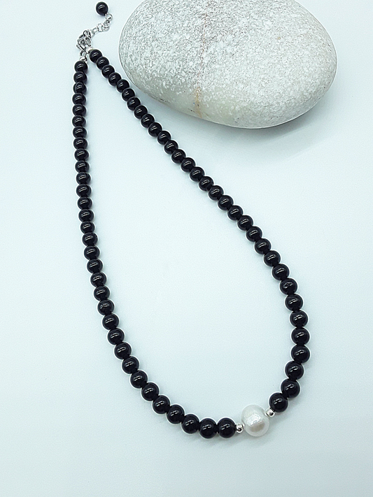 Still Core Necklace by Polmadeva with black onyx beads and single pearl shown in full length beside natural stone
