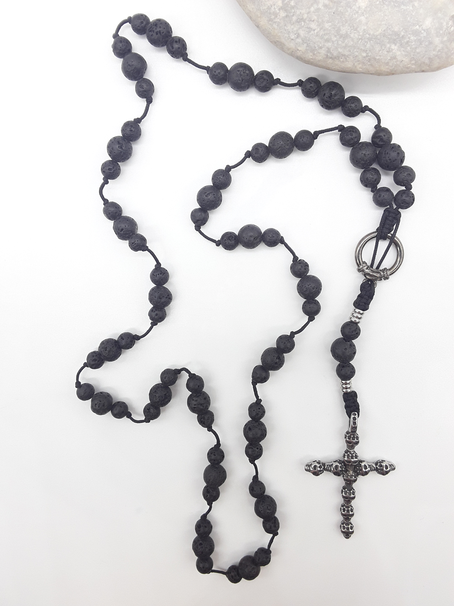 Catholic lava stone rosary with skull crucifix placed beside natural stone on white surface