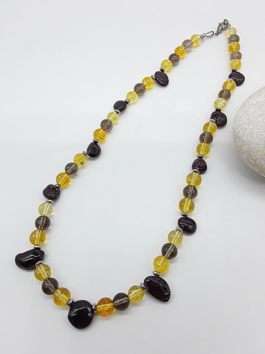 Gemstone necklace featuring citrine, garnet, smoked quartz, and hematite displayed beside a smooth white stone.