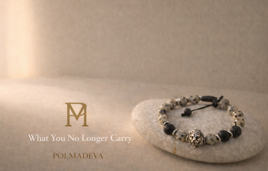 A softly lit Polmadeva bracelet resting on a stone surface, accompanied by the title “What You No Longer Carry” and the Polmadeva logo, evoking calm, release, and quiet presence.