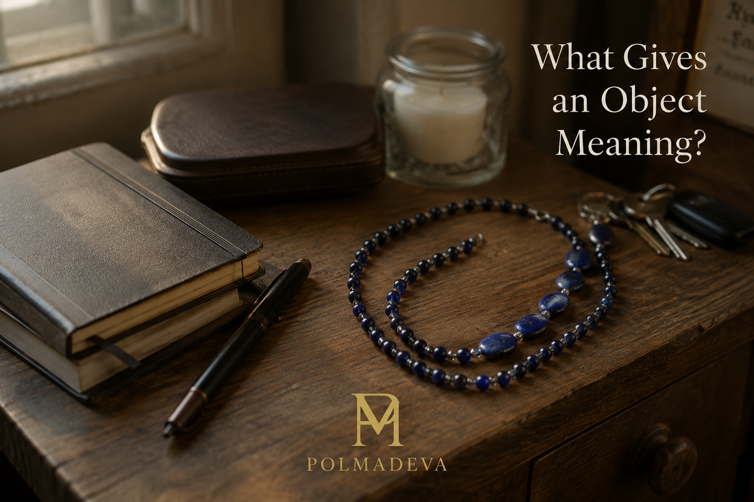 Editorial lifestyle scene of a Polmadeva bracelet resting naturally on a wooden desk beside a notebook, pen, candle, glasses, and keys, with the text “What Gives an Object Meaning?” and the POLMADEVA logo in warm natural light.