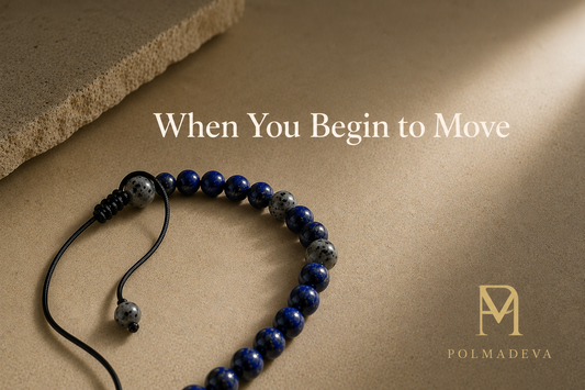 Bracelet arranged in an open curved form on a warm stone surface with soft directional light, titled “When You Begin to Move”, Polmadeva logo bottom right.
