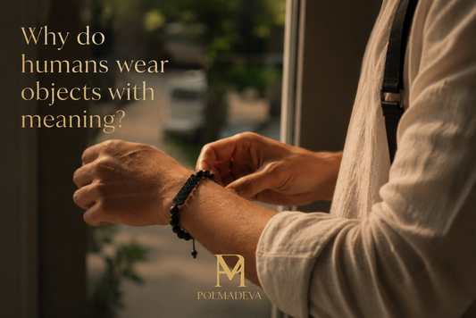 A close, natural moment of a person adjusting a bracelet on their wrist in soft daylight, with the text “Why do humans wear objects with meaning?” and the Polmadeva logo.