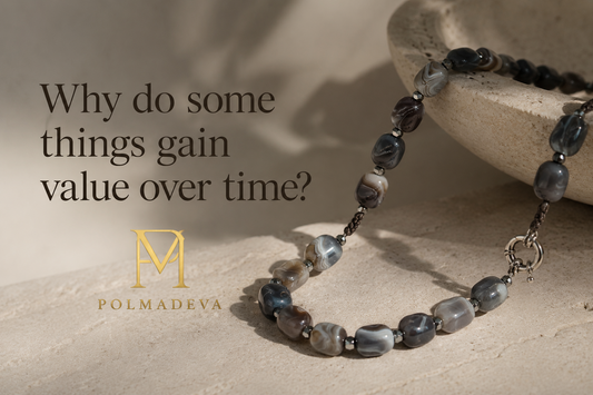 A minimalist, softly lit composition featuring a Polmadeva beaded necklace resting on a natural stone surface, with the title “Why do some things gain value over time?” and the Polmadeva logo, evoking a sense of timeless value and quiet presence.