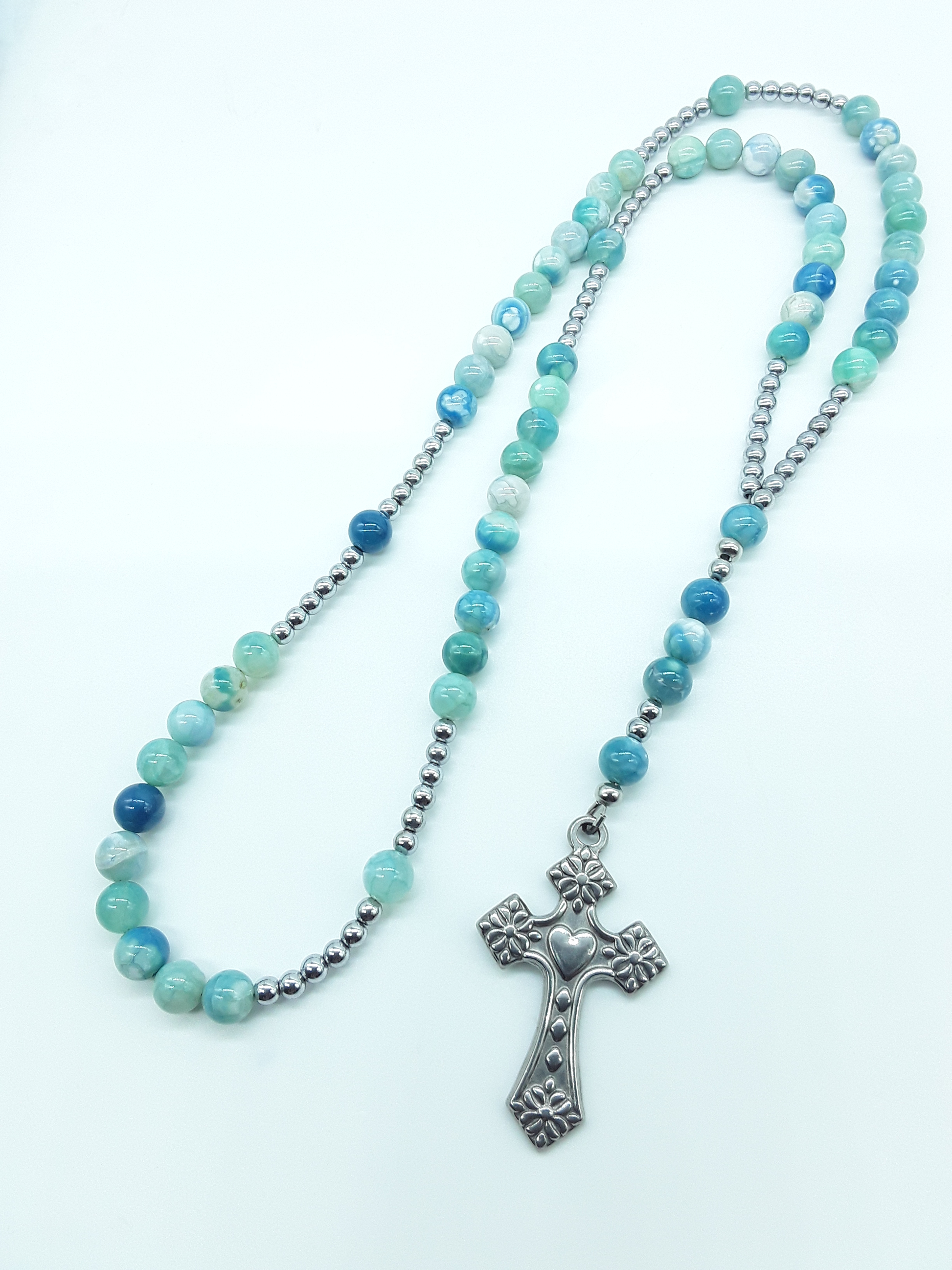 Catholic rosary with natural agate beads, hematite elements, and a stainless steel heart-shaped cross shown in full length on a light background.
