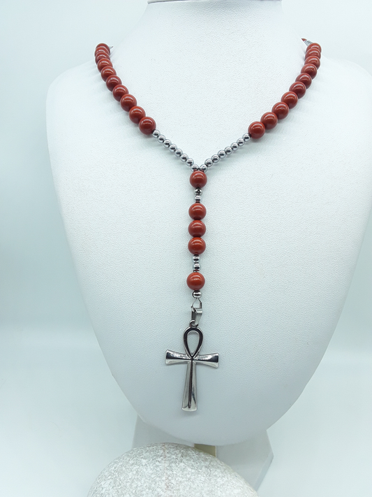 Traditional Catholic rosary made with red jasper beads, hematite spacers, and a stainless steel Ankh cross, displayed on a white bust.

