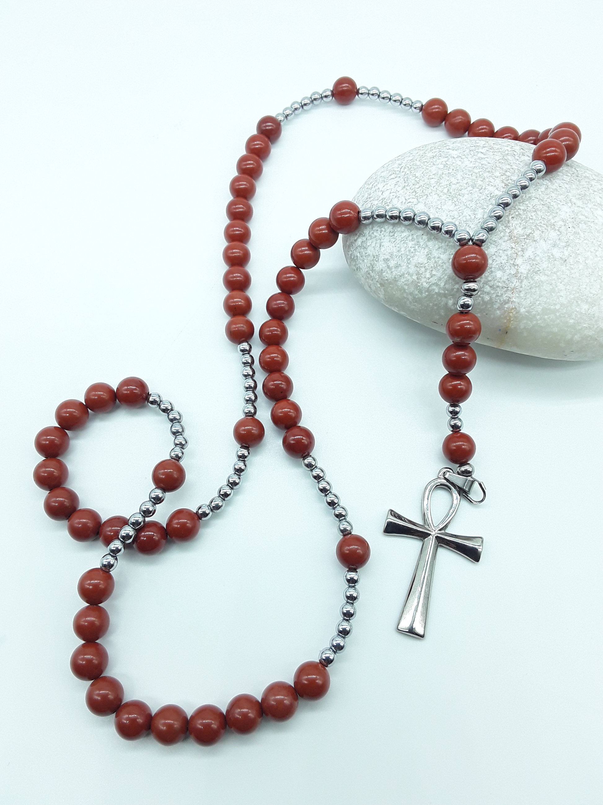 Detail view of a stainless steel Ankh cross attached to a traditional Catholic rosary with red jasper beads.
