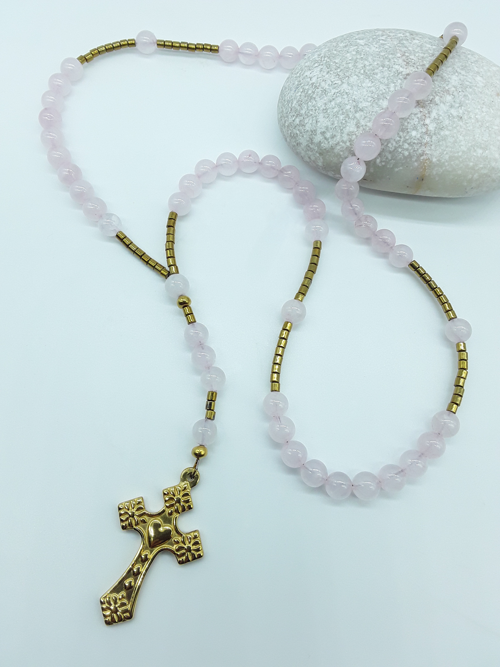 Detail view of a stainless steel heart-shaped cross attached to a traditional Catholic rosary with rose quartz beads.
