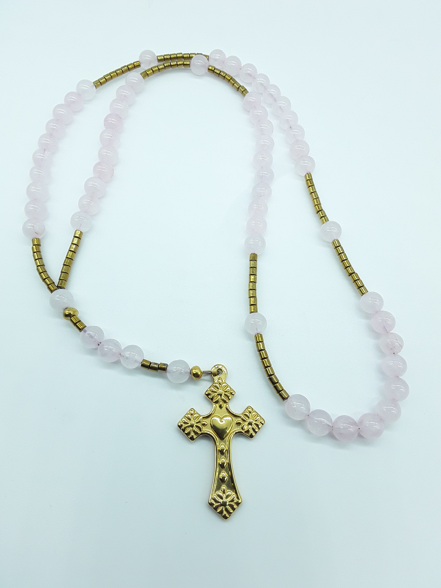 Catholic rosary crafted with rose quartz beads and hematite spacers, featuring a stainless steel heart-shaped cross on a light background.
