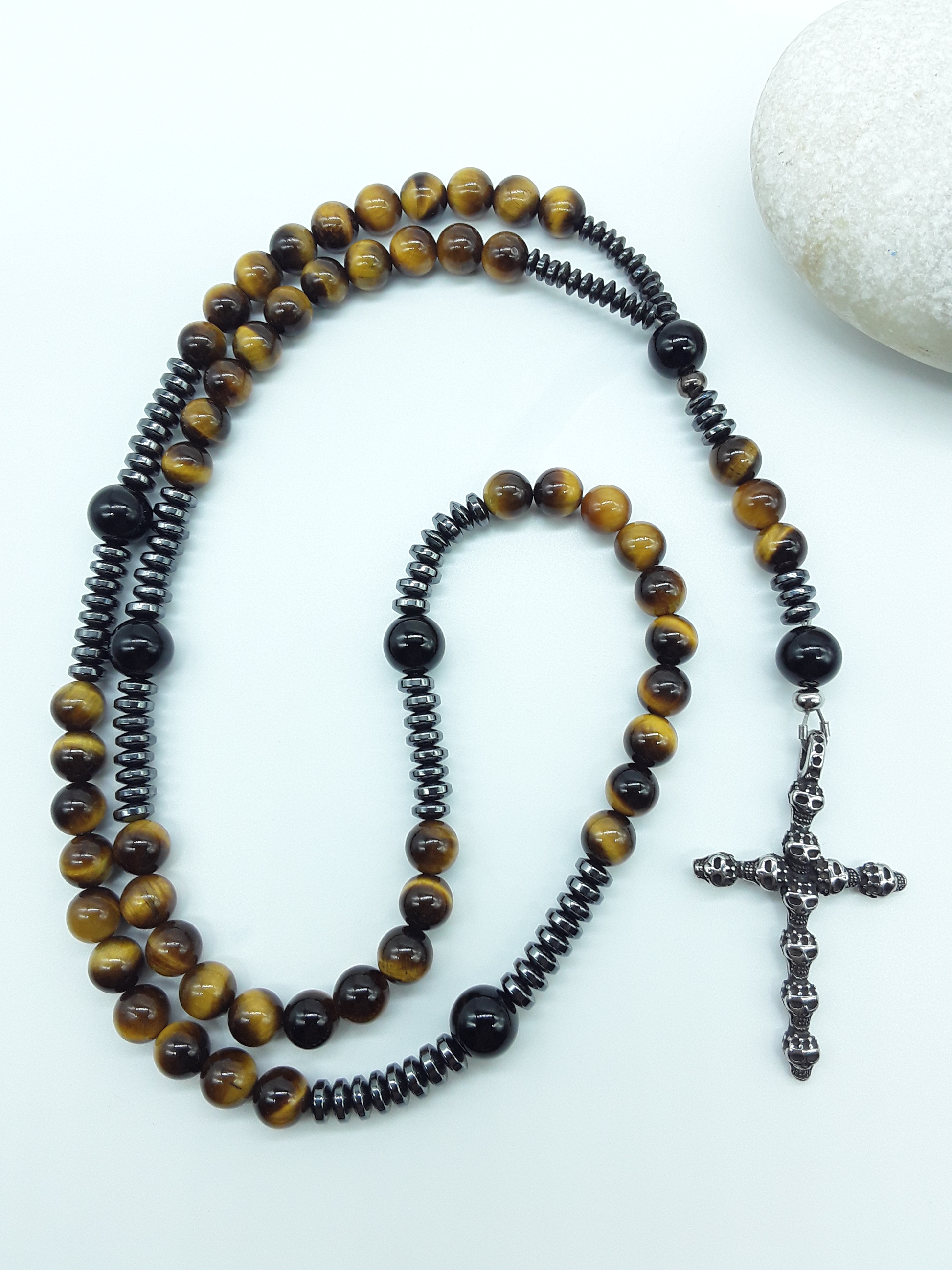 Detail view of a stainless steel skull cross attached to a traditional Catholic rosary with tiger’s eye and black onyx beads.