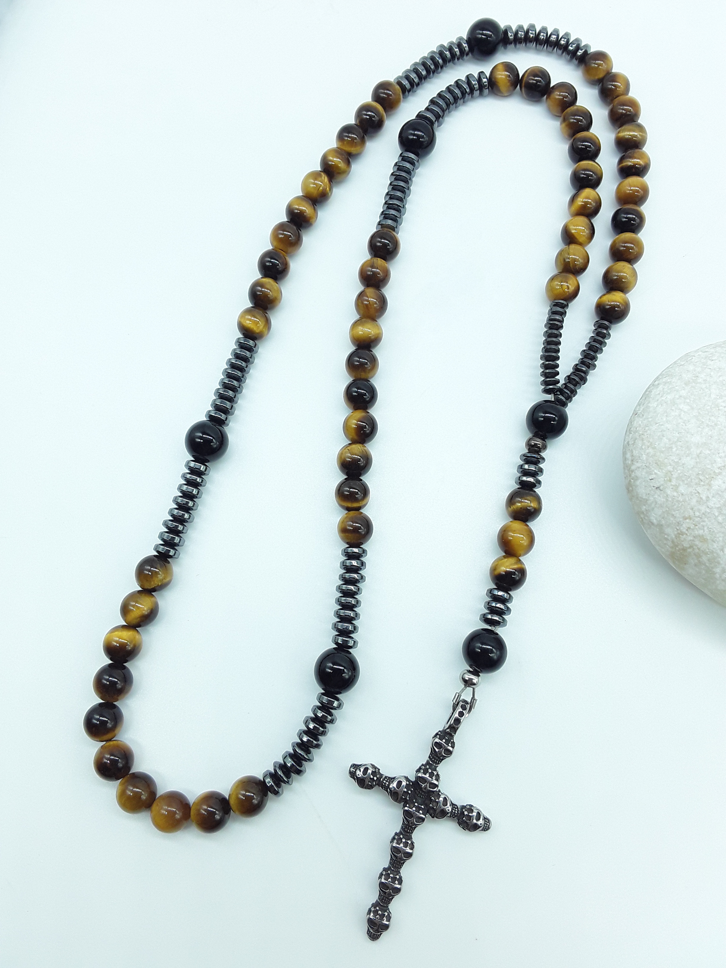 Detail view of a stainless steel skull cross attached to a traditional Catholic rosary with tiger’s eye and black onyx beads.