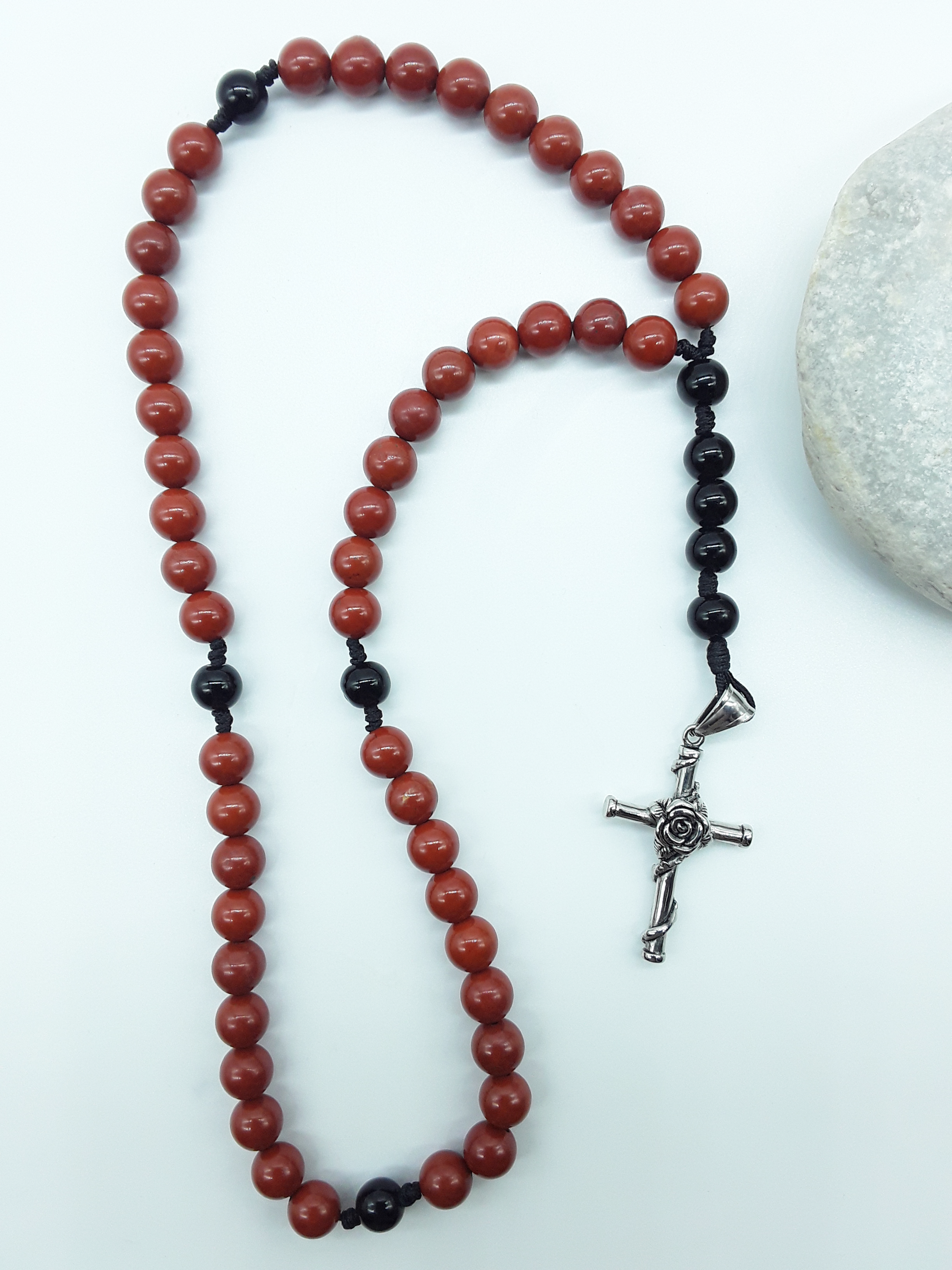Red Jasper and Black Onyx pocket rosary displayed beside a natural stone, highlighting texture and compact form.