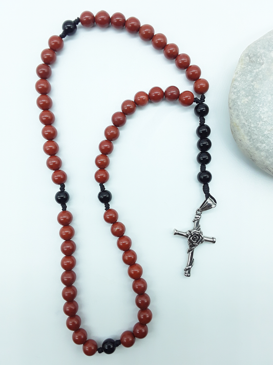 Red Jasper and Black Onyx pocket rosary displayed beside a natural stone, highlighting texture and compact form.