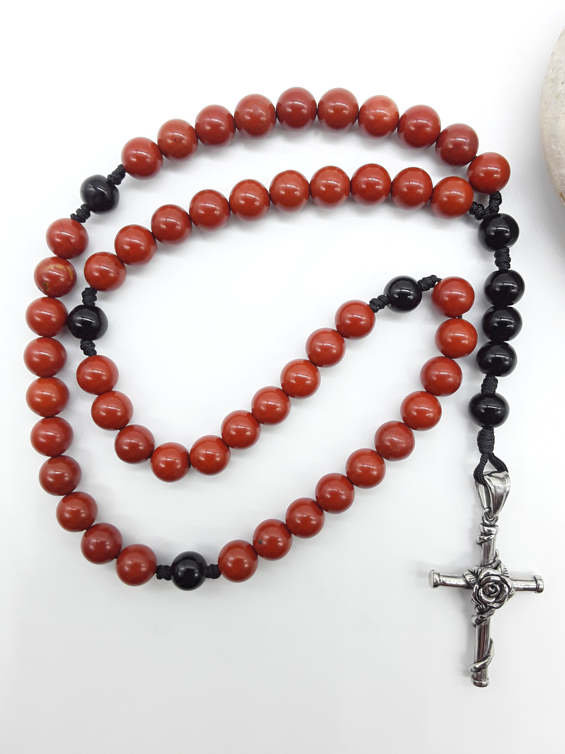 Red Jasper and Black Onyx pocket rosary displayed beside a natural stone, highlighting texture and compact form.