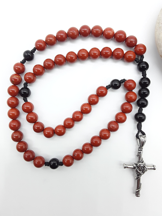 Red Jasper and Black Onyx pocket rosary displayed beside a natural stone, highlighting texture and compact form.