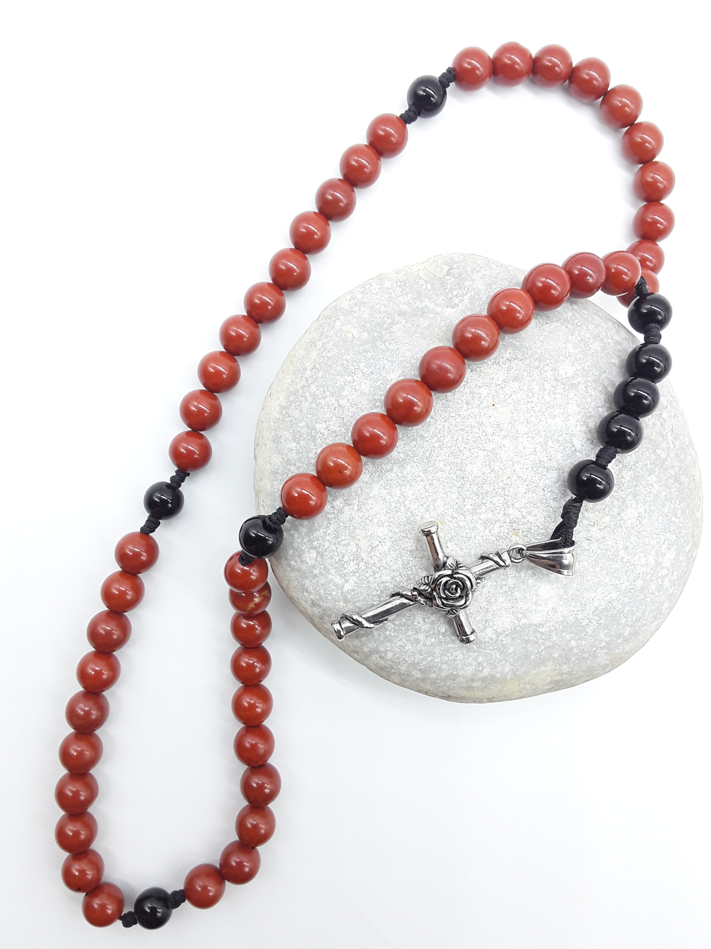 Red Jasper and Black Onyx pocket rosary displayed over a natural stone, highlighting texture and compact form.