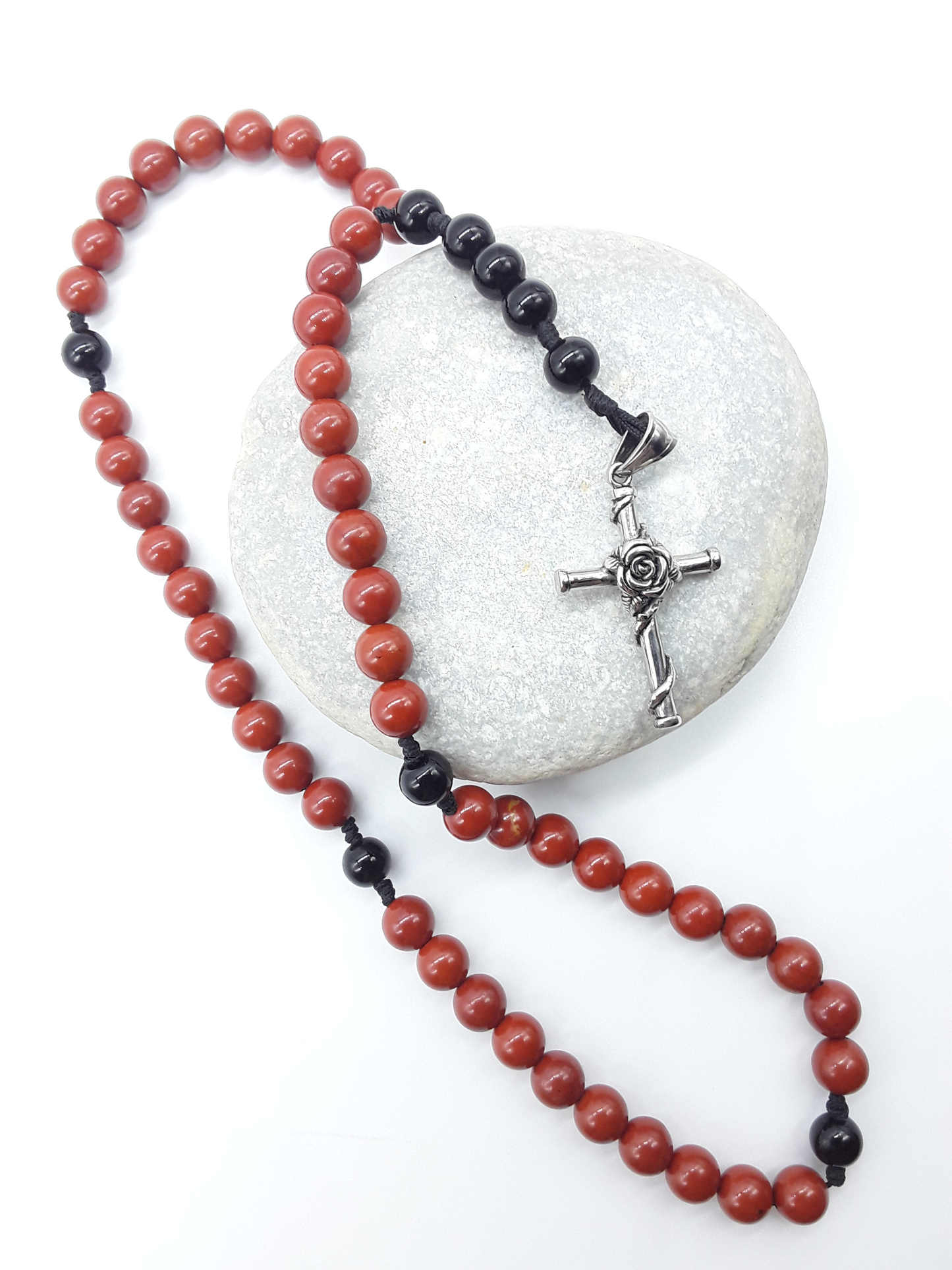 Red Jasper and Black Onyx pocket rosary displayed over a natural stone, highlighting texture and compact form.