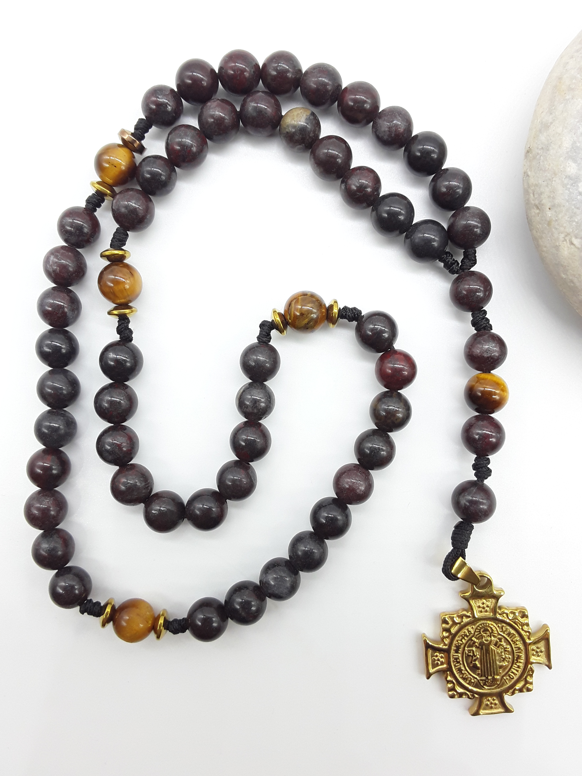 Bloodstone pocket Catholic rosary with Saint Benedict cross placed beside natural stone