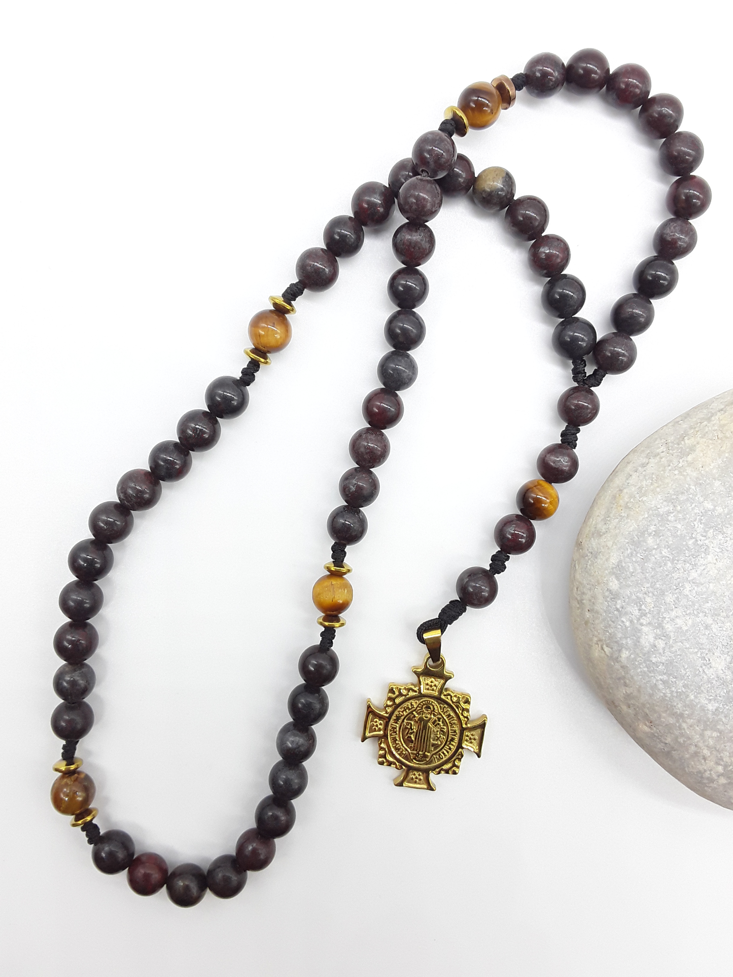 Bloodstone pocket Catholic rosary with Saint Benedict cross placed beside natural stone