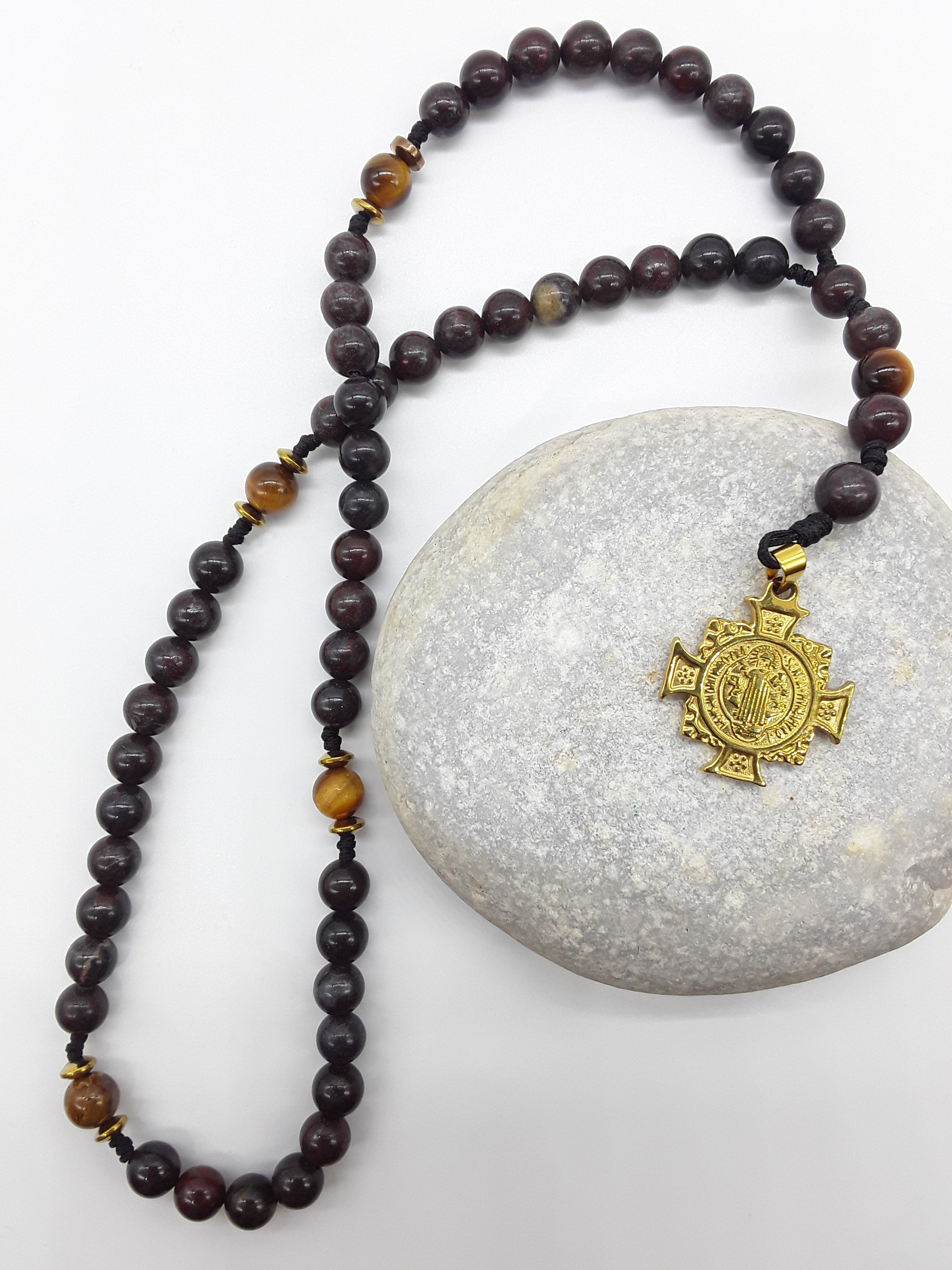 Handmade Bloodstone pocket rosary with Saint Benedict crucifix resting on stone surface