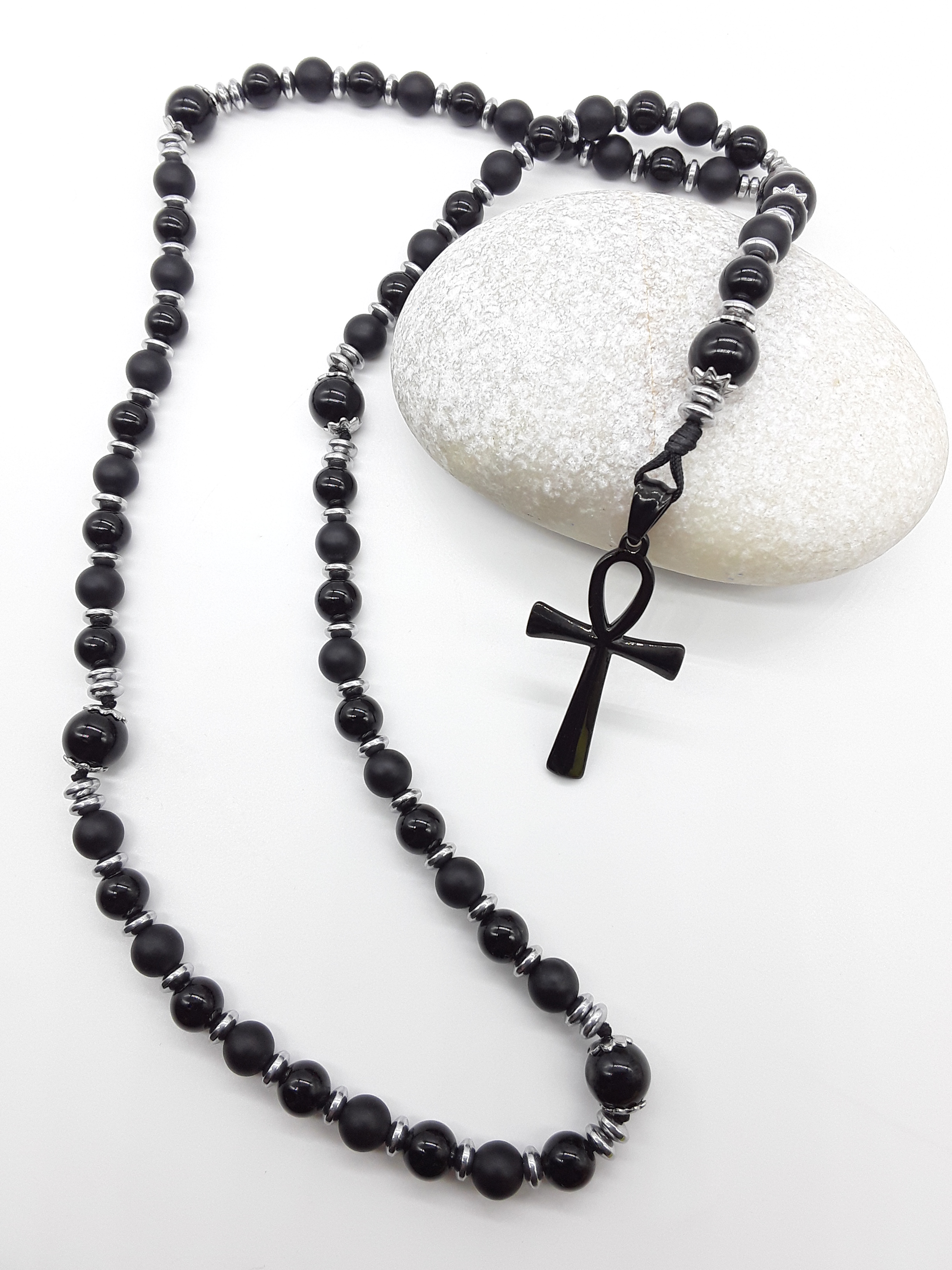 Onyx, Hematite and Agate Catholic Rosary with black stainless steel Ankh cross by Polmadeva resting on natural stone surface.