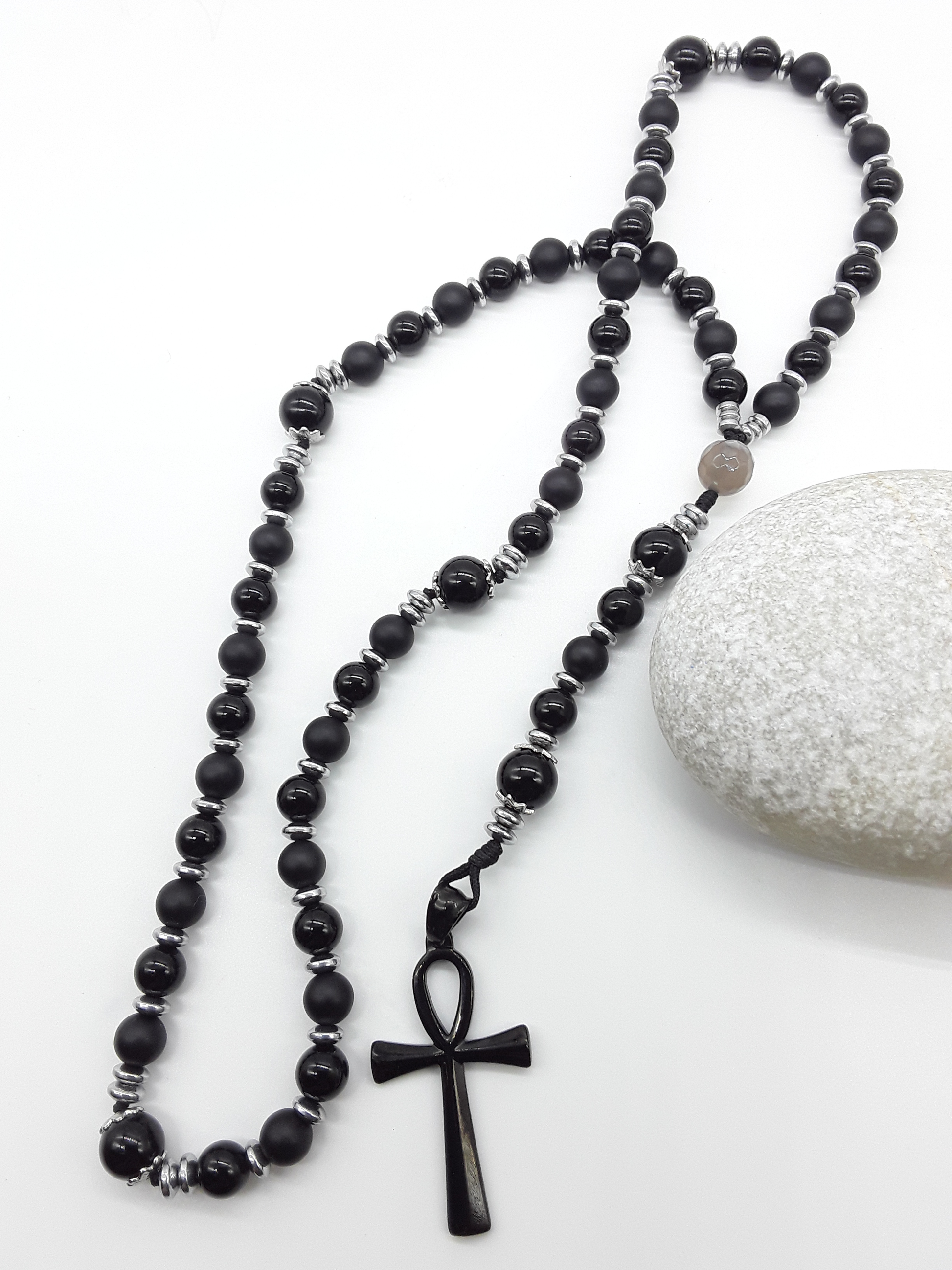 Onyx and Hematite Ankh Catholic Rosary (5 Decade) by Polmadeva placed beside natural stone with black cross.