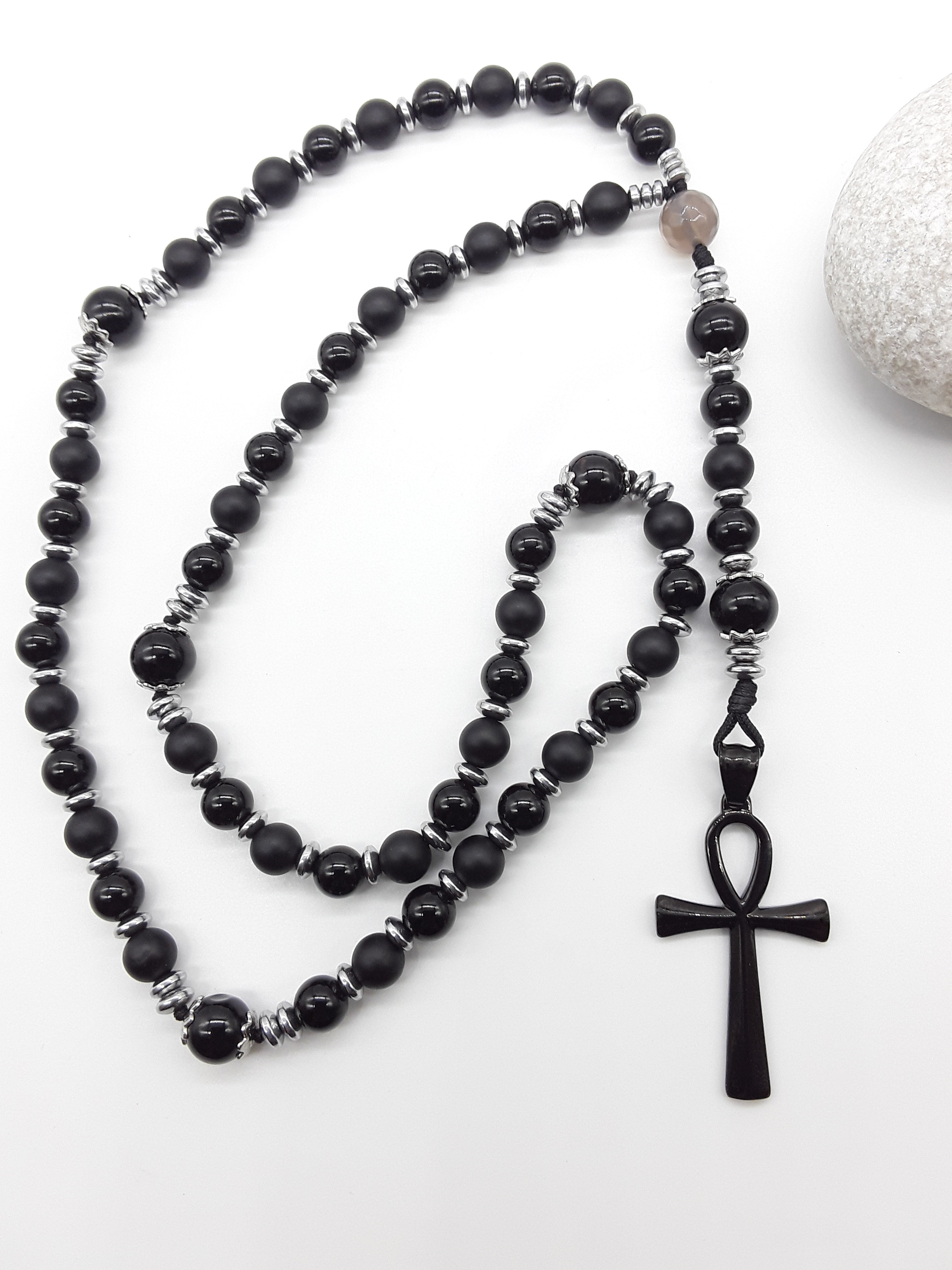 Onyx and Hematite Ankh Catholic Rosary (5 Decade) by Polmadeva placed beside natural stone with black cross.