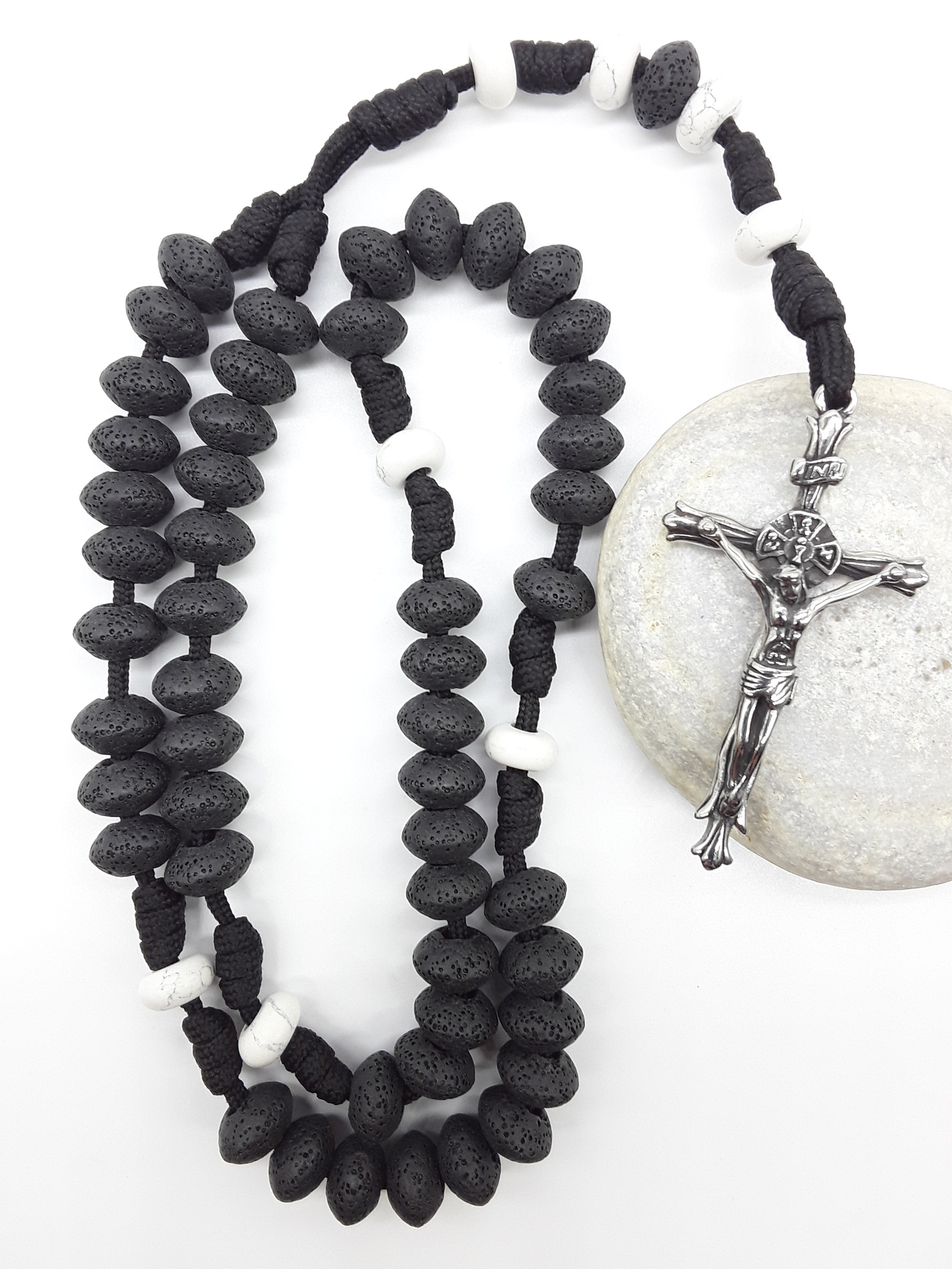 Lava and Howlite Paracord Catholic Rosary (5 Decade) by Polmadeva resting on natural stone surface with stainless steel crucifix.