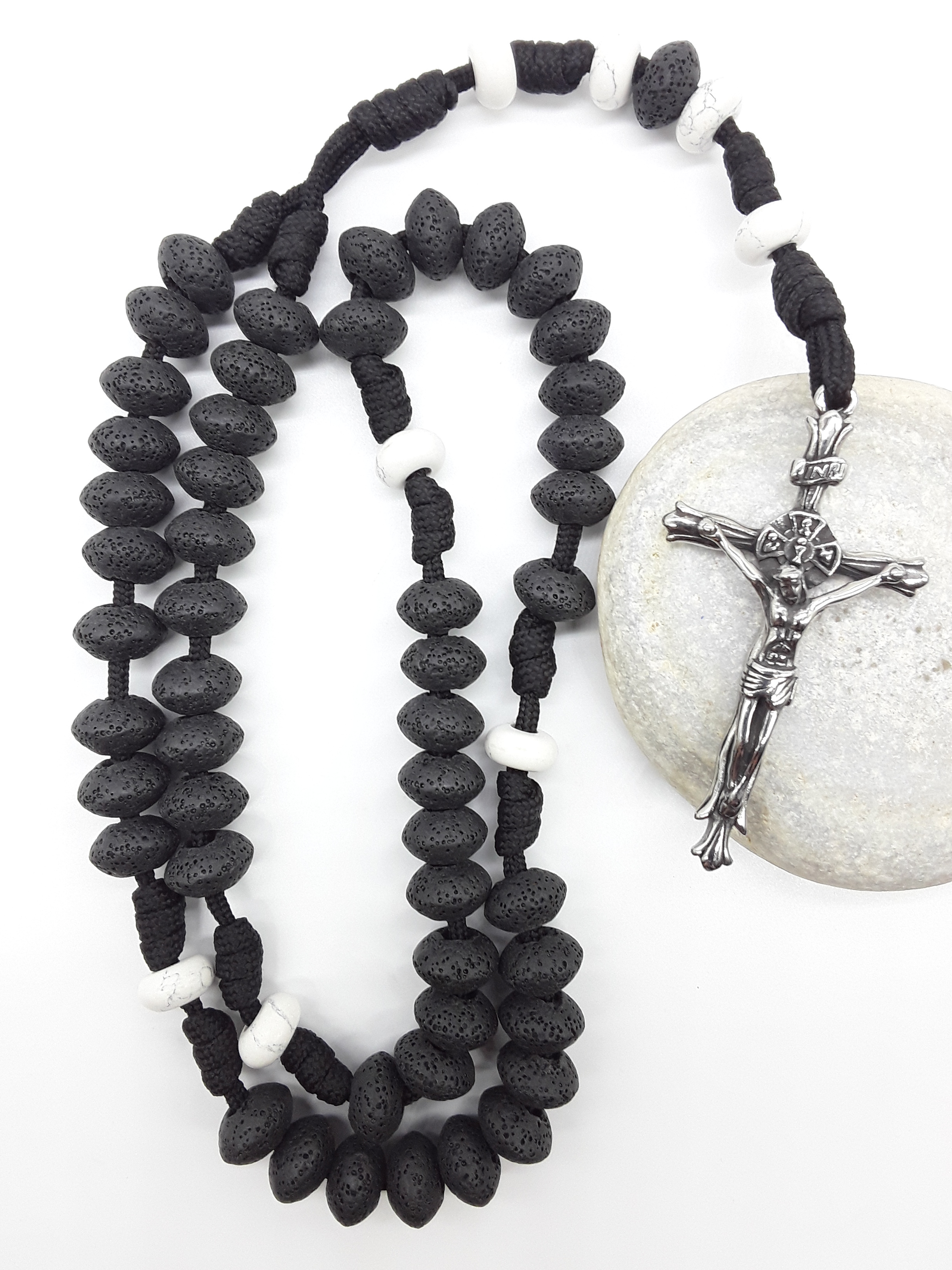 Lava and Howlite Paracord Catholic Rosary (5 Decade) by Polmadeva resting on natural stone surface with stainless steel crucifix.