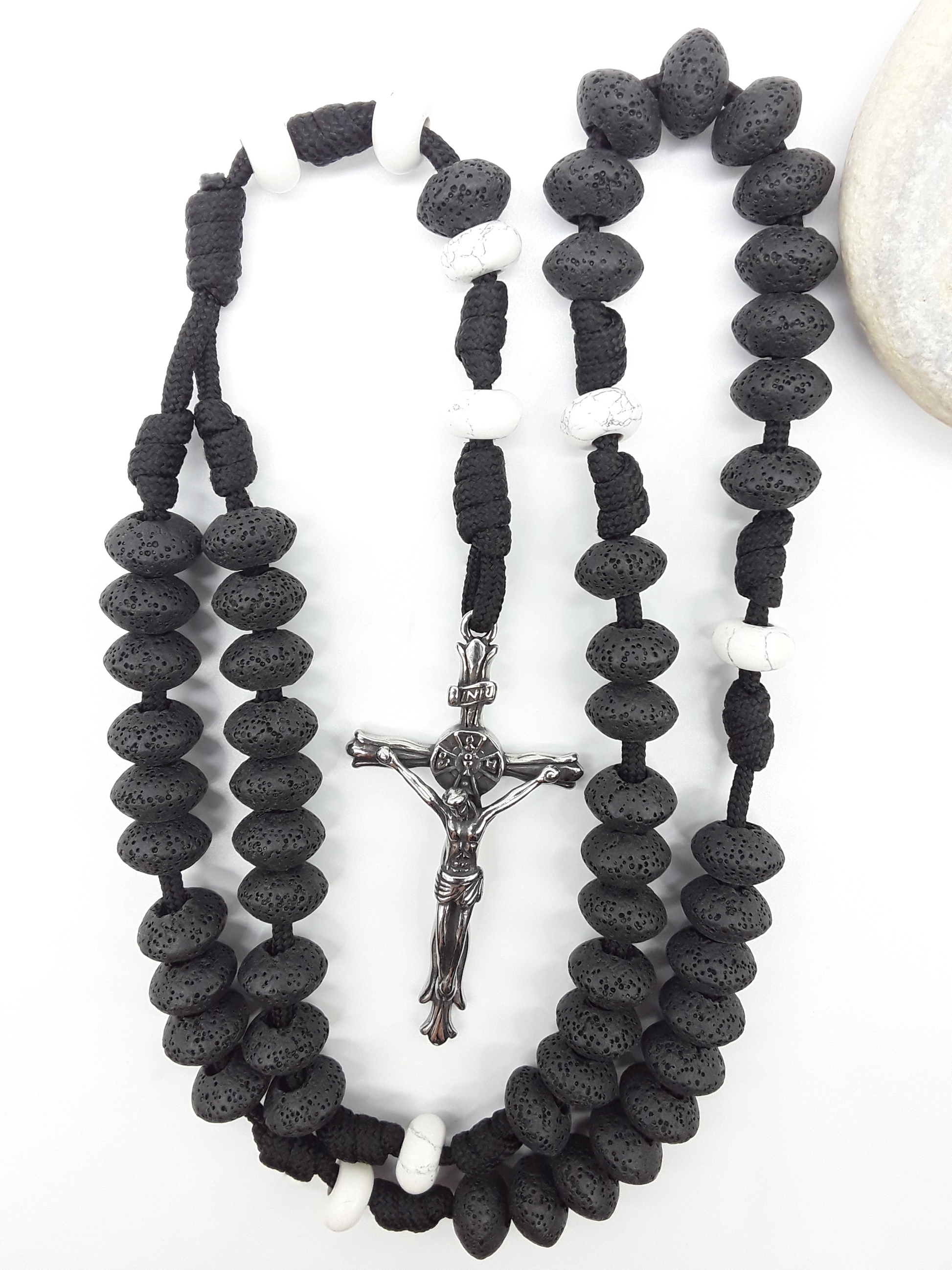 Lava and Howlite Paracord Catholic Rosary (5 Decade) by Polmadeva placed beside natural stone with stainless steel crucifix.