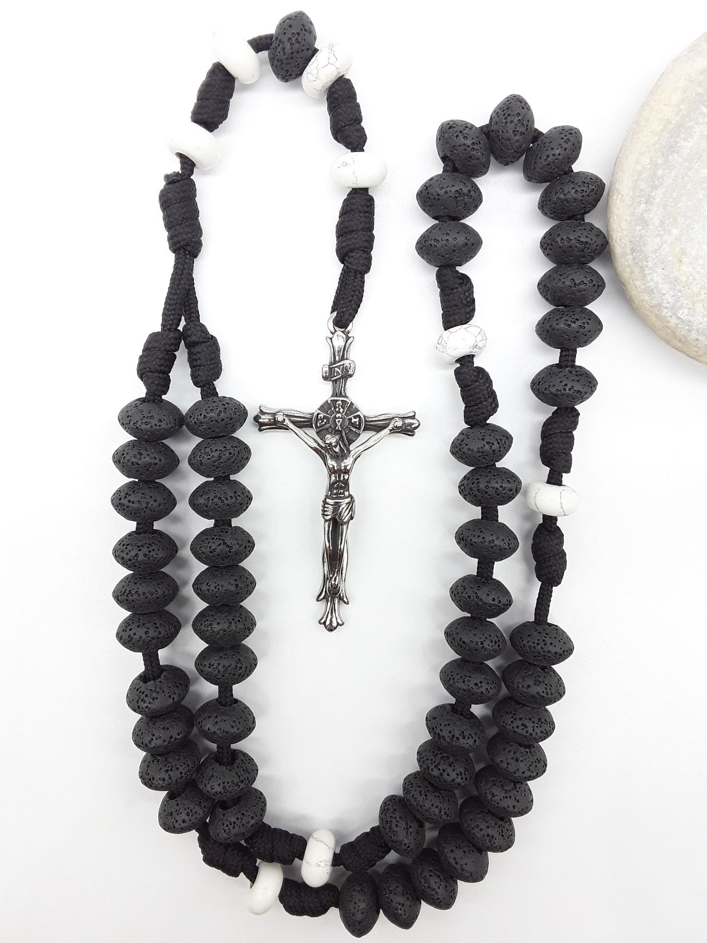 Lava and Howlite Paracord Catholic Rosary (5 Decade) by Polmadeva placed beside natural stone with stainless steel crucifix.