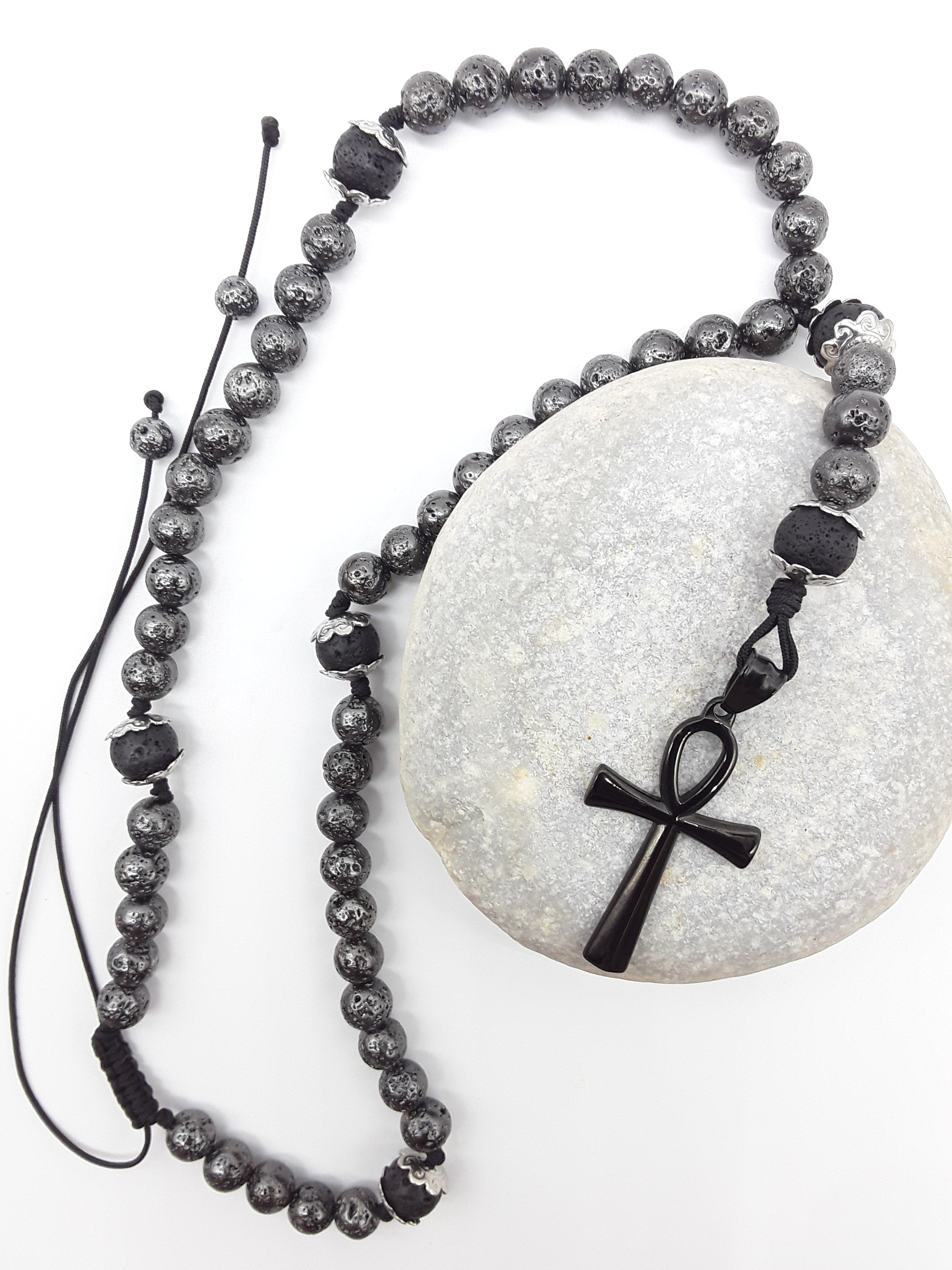 Galvanized Lava Ankh Catholic Rosary with black stainless steel Ankh cross by Polmadeva resting on natural stone surface.