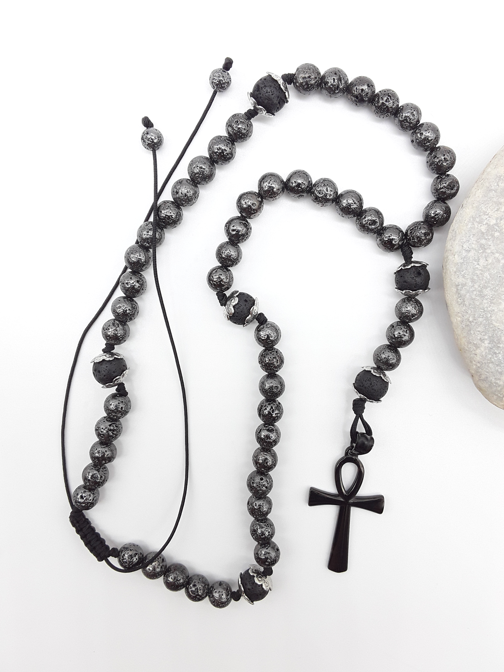 Galvanized Lava Ankh Catholic Rosary (5 Decade) by Polmadeva placed beside natural stone with black stainless steel cross.