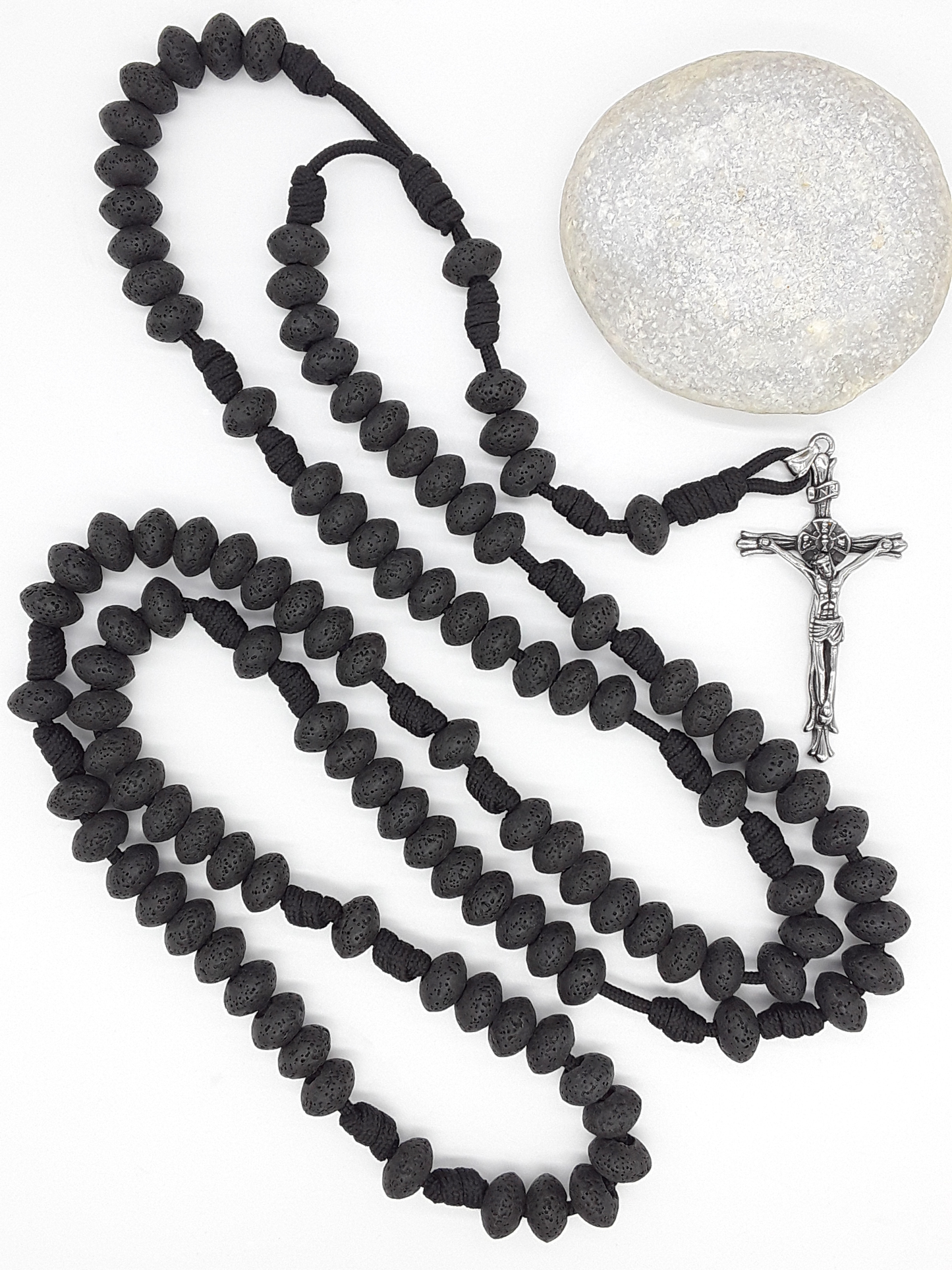 Lava stone Catholic Paracord Rosary placed beside natural stone, expressing endurance, weight, and grounded prayer through repetition