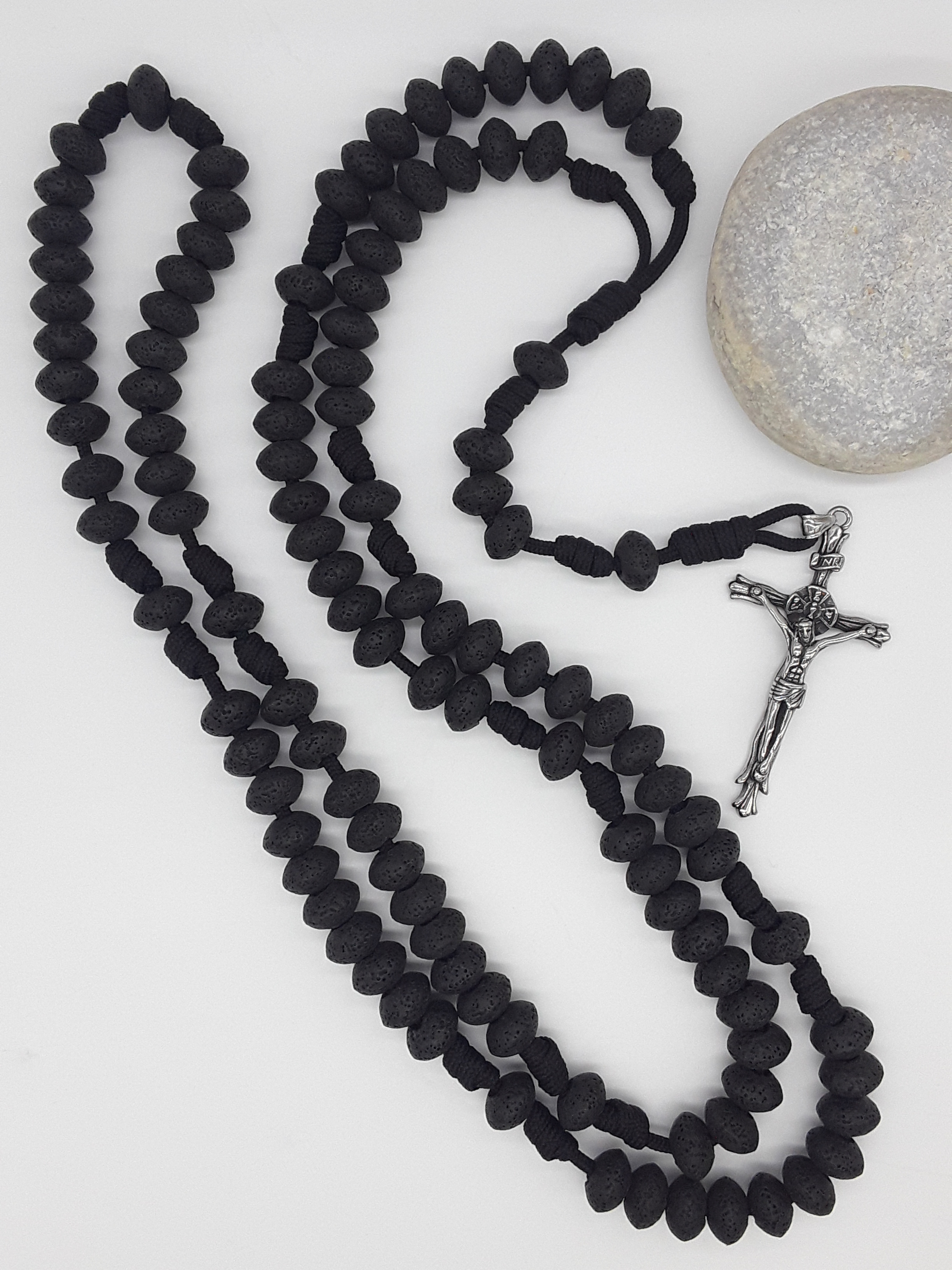 Lava stone Catholic Paracord Rosary placed beside natural stone, expressing endurance, weight, and grounded prayer through repetition